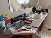 Bathroom counter with assortment of toiletry bags, manicure set, mirrors, combs, and cleaning wipes by the sink with a faucet