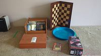 Overview photo showing wooden box with CDs, chess/checkers board, blue tray, and two wooden boxes arranged on carpeted floor.