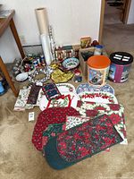 Photo showing assorted Christmas decor including silver jingle bell wreath, table mats with holiday motifs, rolls of wrapping paper, and ribbon spools.