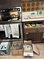 Large vintage Canadian General Electric slow cooker sitting on stove next to a box of glass shrimp bowls and white food steamer insert on countertop with a drawer of utensils partially open nearby.