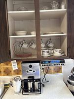 Photo of cabinet shelf with Royal Doulton cups and saucers, coffee machine on countertop beneath