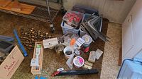 Wide shot showing an assortment of cupboard pulls, hinges, screws, and other hardware items scattered on a carpet with boxes and containers in the background.