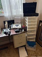 Office corner showing Brother FAX-565 fax machine, telephones, black briefcase, metal filing cabinet, 8-drawer plastic storage cabinet, file holders and office supplies on tabletop and floor