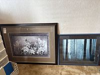 Two framed prints leaning against a wall on the floor, showing the designs and frames of both prints.
