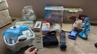 Photo of various health and beauty items including electric foot baths, boxes, braces, heating pad, and warming devices laid on carpet.