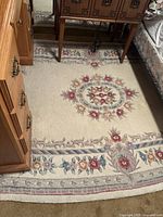 Full view showing the floral patterned rug with central medallion and border design in soft colors including cream, red, blue, and green.