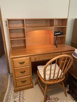 Full view of oak desk with hutch, working light on, and chair