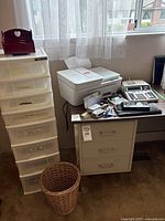 Photo showing HP DeskJet printer on a desk, 8-drawer plastic storage cabinet to the left, two calculators, various office supplies, vintage leather bill file, filing cabinet beneath printer, and wicker wastebasket on floor.