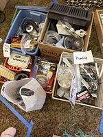 Top view of assorted plumbing supplies in bins and boxes including washers, fittings, cables, and tap parts.