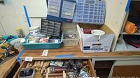 Overview of table with hardware trays, multiple drawers containing screws, nails, and wooden dowels, also drawer pulls and table legs visible.