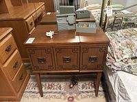 Wooden sewing machine cabinet with drawers and decorative front panels, showing the overall unit where machine is housed.