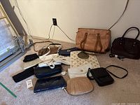 Photo showing various women's handbags and clutches in different colors and sizes laid on carpeted floor.