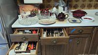 Overview of kitchen items on a counter and drawers including serving dishes, teapot, blender, and cutlery drawers open showing contents