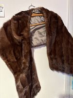 Brown mink fur stole hanging on wooden hanger, showing full stole length and fur texture.