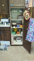 Open cabinet with shelves holding vintage Tupperware bowls, assorted dishes, pots and a kitchen scale visible on a shelf.