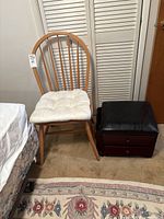 Wooden chair with white padded seat cushion and dark wood storage stool with black cushioned top on casters side by side.