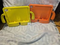 Photo showing two kids tablet holders, one yellow and one orange, side by side on a white surface.