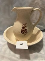 Antique cream ceramic pitcher with brown floral decoration on side and matching basin under it.