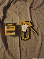 Photo of DeWalt multi-tacker stapler and box of Tacs staples on cloth surface.