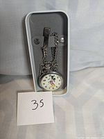 Front view of silver Fossil Mickey Mouse pocket watch on chain with clip in grey and white box, white paper with '35' for lot reference.