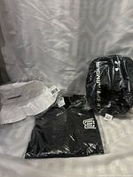 Photo showing three brand new sealed items: white Warrior bucket hat, black Sherwood Hockey T-shirt size Large, and black Under Armour shower bag.