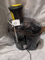 Front view of the Jack LaLanne Fusion Juicer showing overall black design with clear lid, metal locking arm, and power cord.