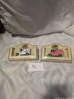 Two Lledo model cars in original box packaging side-by-side against fabric background