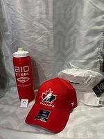 The photo shows three brand new hockey gear items: a red Bio Steel water bottle, a red adjustable Team Canada Hockey Fanatics hat with a maple leaf hockey logo, and a white Warrior bucket hat still in plastic wrap.
