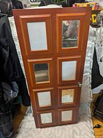 Front view of the standing wooden jewelry box showing the eight-panel door with mirrors and empty picture frames arranged in a grid pattern.