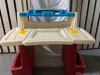 Front view of the Step 2 kids desk showing the blue top part, cream work surface with yellow holders, and red base storage compartments.