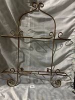 Full view of gold color wall mounted wire plate holder on fabric background showing scroll details and horizontal supports