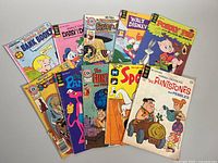Ten vintage comic books laid out in a fan arrangement showing front covers including The Flintstones, Pink Panther, Scooby Doo, Porky Pig, Daisy Duck, Barney Rubble, and others.