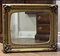 Front angle view of the ornately framed gilt mirror, showing decorative corners and some wear on sides.