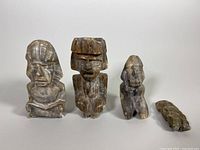Four vintage tiki stone sculptures displayed on white background, showing size differences and styles; largest has visible crack and chips