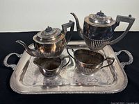 Full view of tea service on tray showing coffee pot, teapot, creamer, sugar bowl, and tray with reflective surface, aged patina visible