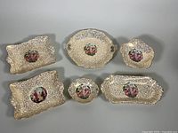 Top-down photo showing all six Royal Winton Grimwades porcelain dishes with Fragonard romantic scenes, varying shapes including rectangular and oval, with ornate raised textured pattern backgrounds.