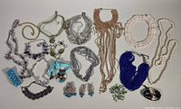 Top-down view of multiple costume jewelry pieces including necklaces, earrings and bracelets arranged on white surface.