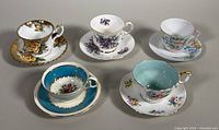 Five assorted Aynsley bone china teacups and saucers displayed together showing floral designs and gold rims.