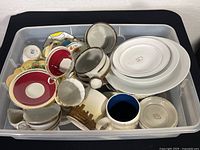 Assorted teacups and saucers in a plastic bin showing variety and condition.