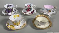 Five assorted bone china teacups and saucers, all floral patterned with varying colors and edging styles.