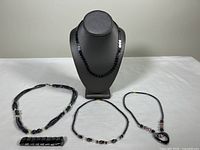 Photo showing four hematite and black stone jewelry pieces arranged on a white table, including necklaces and a stretch bracelet.