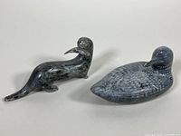 Two soapstone carvings, a loon and a seal, shown side by side on a white surface