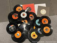 Multiple 45 RPM vinyl records with various label colors and some in sleeves laid out on floor