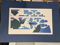 Photo showing the art print with blue mat, art featuring abstract shapes and bird motifs in blue, purple, dark green and white.