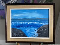 Framed oil painting showing a seascape with crashing blue waves and rocky cliffs, signed Beverly K.