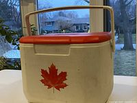 Image showing the full cooler with red lid and maple leaf design on white body, with window background