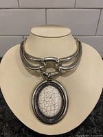 Front view of the silver-toned collar necklace with large oval crackled white stone pendant on display bust.
