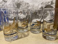 Four collectible Expo 67 glasses in a row, each depicting different pavilion designs with gold, blue, and black accents.