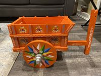 Full view of the orange painted wooden folk art planter wheelbarrow with floral and geometric motifs on its sides and handle.