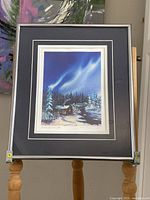 Full image of the framed lithograph showing snowy cabin night scene with aurora sky and mat/frame.